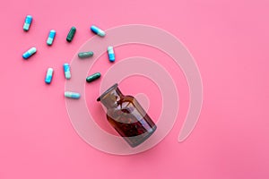 Medicine. Color capsules near pill bottle on pink background top view copy space
