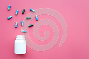 Medicine. Color capsules near pill bottle on pink background top view copy space