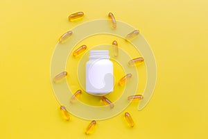 Medicine. Color capsules near pill bottle on yellow background top view copy space