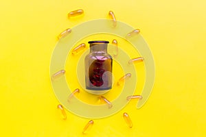 Medicine. Color capsules near pill bottle on yellow background top view copy space