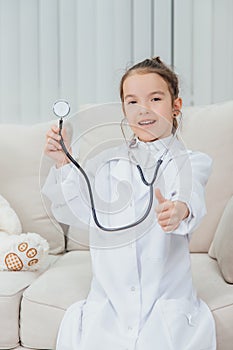 Little girl in medical coat holding a stethoscope, pointing her finger up. photo