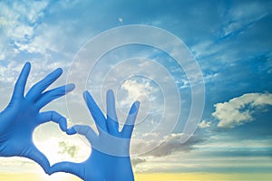 Medicine concept. Doctor hands in blue medical surgical gloves making heart on sky clouds background