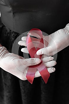 medicine concept - female hands in medical gloves holding red AIDS awareness ribbon.