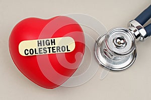 Near the stethoscope lies a heart on which a sticker is pasted with the inscription - High Colesterol photo