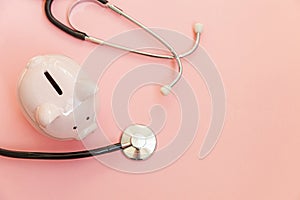 Medicine doctor equipment stethoscope and piggy bank isolated on pink pastel background. Health care financial checkup or saving