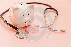 Medicine doctor equipment stethoscope and piggy bank isolated on pink pastel background. Health care financial checkup or saving