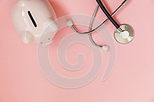 Medicine doctor equipment stethoscope and piggy bank isolated on pink pastel background. Health care financial checkup or saving