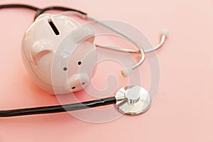 Medicine doctor equipment stethoscope and piggy bank isolated on pink pastel background. Health care financial checkup or saving