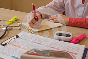 Medicine doctor`s working table. Healthcare concept. Female medical doctor writing something sitting at her office