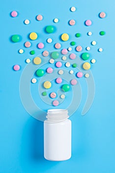 Medicine green, yellow and pink pills or capsules and white bottle on a blue background
