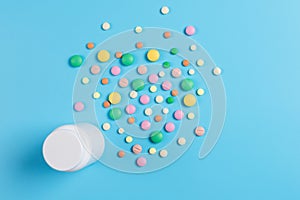 Medicine green, yellow and pink pills or capsules and white bottle on a blue background