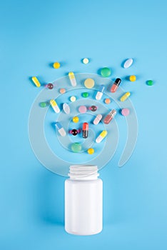 Medicine green, yellow and pink pills or capsules and white bottle on a blue background