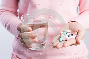 Medicine, health care and people concept - close up of woman taking in pill and another hand holding a glass of clean mineral