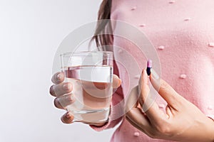 Medicine, health care and people concept - close up of woman taking in pill and another hand holding a glass of clean mineral