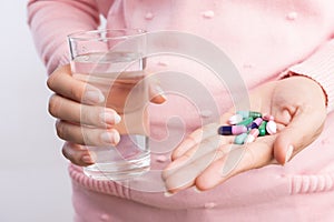 Medicine, health care and people concept - close up of woman taking in pill and another hand holding a glass of clean mineral