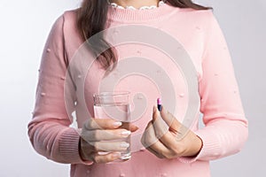 Medicine, health care and people concept - close up of woman taking in pill and another hand holding a glass of clean mineral