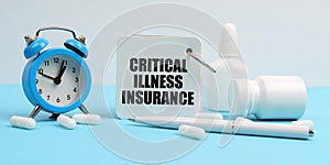 On a blue surface lie pills, an alarm clock and a notebook with the inscription - Critical Illness Insurance photo