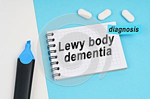 On a white and blue surface are pills, a marker and a notebook with the inscription - Lewy body dementia photo