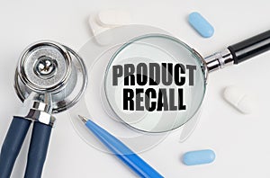 On a white surface lie pills, a pen, a stethoscope and a magnifying glass with the inscription - PRODUCT RECALL photo