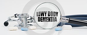 On a white surface are pills, a stethoscope and a magnifying glass inside which is written - Lewy body dementia photo