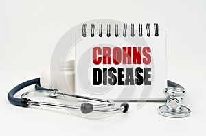 On a white table lies a stethoscope, pills and a notebook with the inscription - CROHNS DISEASE photo