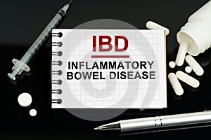 On the black surface are pills, a syringe and a notebook with the inscription - IBD-Inflammatory Bowel Disease