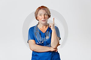 Medicine, healthcare and coronavirus concept. Thoughtful redhead middle-aged nurse, doctor in scrubs have assumption or