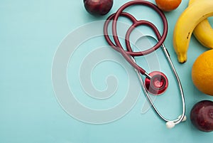 Medicine and healthcare, nutrition or medical insurance over blue background. Fruits and red sthetoscop. Copy space.