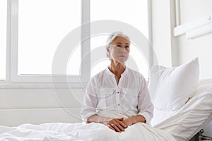 Sad senior woman sitting on bed at hospital ward