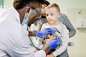 Medicine, healthcare, pediatry and people concept - happy woman with her son and African American doctor with