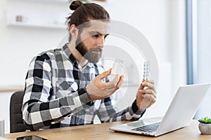 Medicine held by Caucasian young man looking through information on laptop.