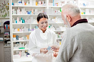 Smiling young female pharmacist giving prescription medication pills to senior male patient photo