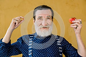 Medicine, pills vs healthy food and fruits. Stylish smiling bearded senior men holding red pill in one hand and red