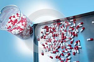 Medicine red white capsules on on stainless steel tray and inside Laboratory glassware blue background white spotlight