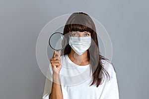 Medicine and research. A woman doctor in a coat and with a mask on her face holding a magnifying glass. Copy space
