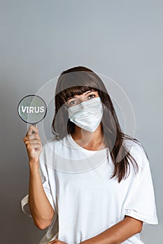 Medicine and research. A woman doctor in a coat and with a mask on her face holding a magnifying glass. Copy space. Vertical