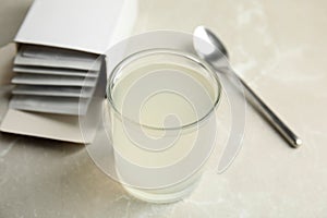 Medicine sachets, glass of water and spoon on light table