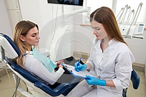 Medicine, stomatology and health care concept - close up of dentist with clipboard and happy patient woman at dental clinic