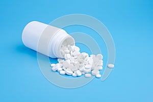 Medicine white pills drop out of the white bottle on blue background