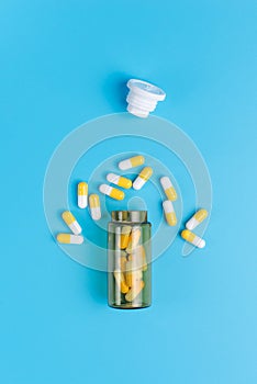 Medicine white and yellow pills drop out of the brown glass bottle on blue background