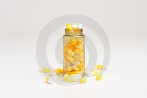 Medicine white and yellow pills or tablets drop out of the brown glass bottle on white background