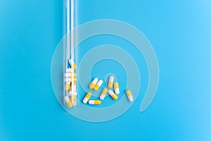 Medicine white and yellow pills or tablets drop out of the test tube on blue background