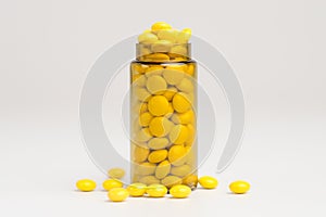 Medicine yellow pills drop out of the brown glass bottle on white background