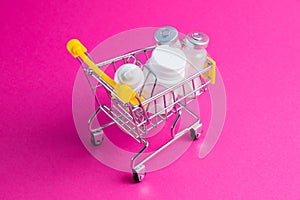 Medicines, drops in a metal trolley for a buyer from a supermarket on a pink paper background. The concept of medicine and the