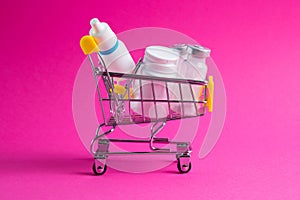 Medicines, drops in a metal trolley for a buyer from a supermarket on a pink paper background. The concept of medicine and the