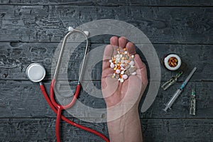 Medicines and a man's hand with a handful of pills on a wooden background