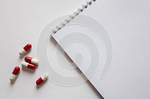 Medicines, pills red-white capsules on a white background with a doctor's working table, blank medical record