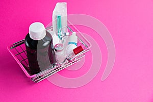 Medicines in a shopping cart for a supermarket shopper on a pink paper background. The concept of medicine and the cost of