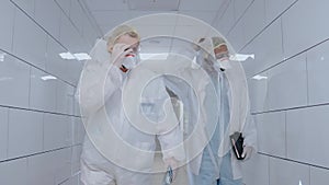 Medics take off protective suits and masks while walking in white hospital hall