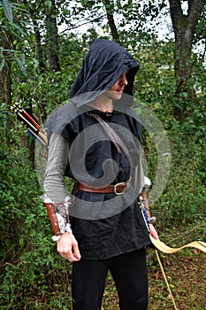 Medieval archer with black hood and coloured arrows in the quiver stands with bow